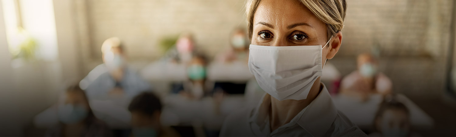 Female teacher wearing a face mask while teaching children at elementary school and looking at camera