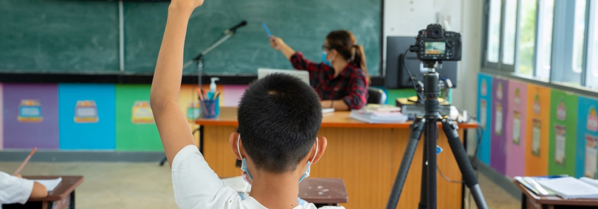 child raising hand in classroom set up for hybrid learning due to pandemic