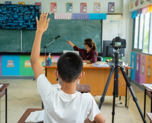 child raising hand in classroom set up for hybrid learning due to pandemic